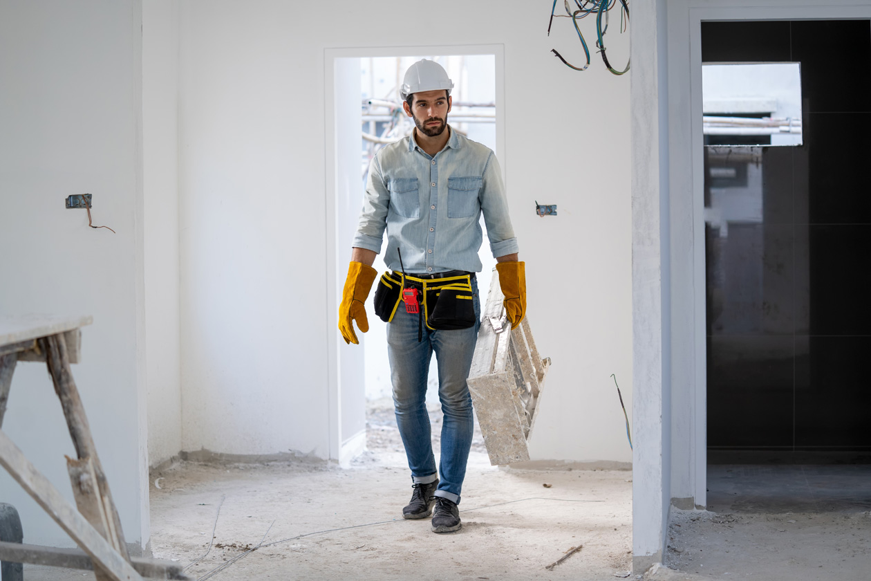 Handyman wearing safety gear carrying tools while performing building maintenance tasks