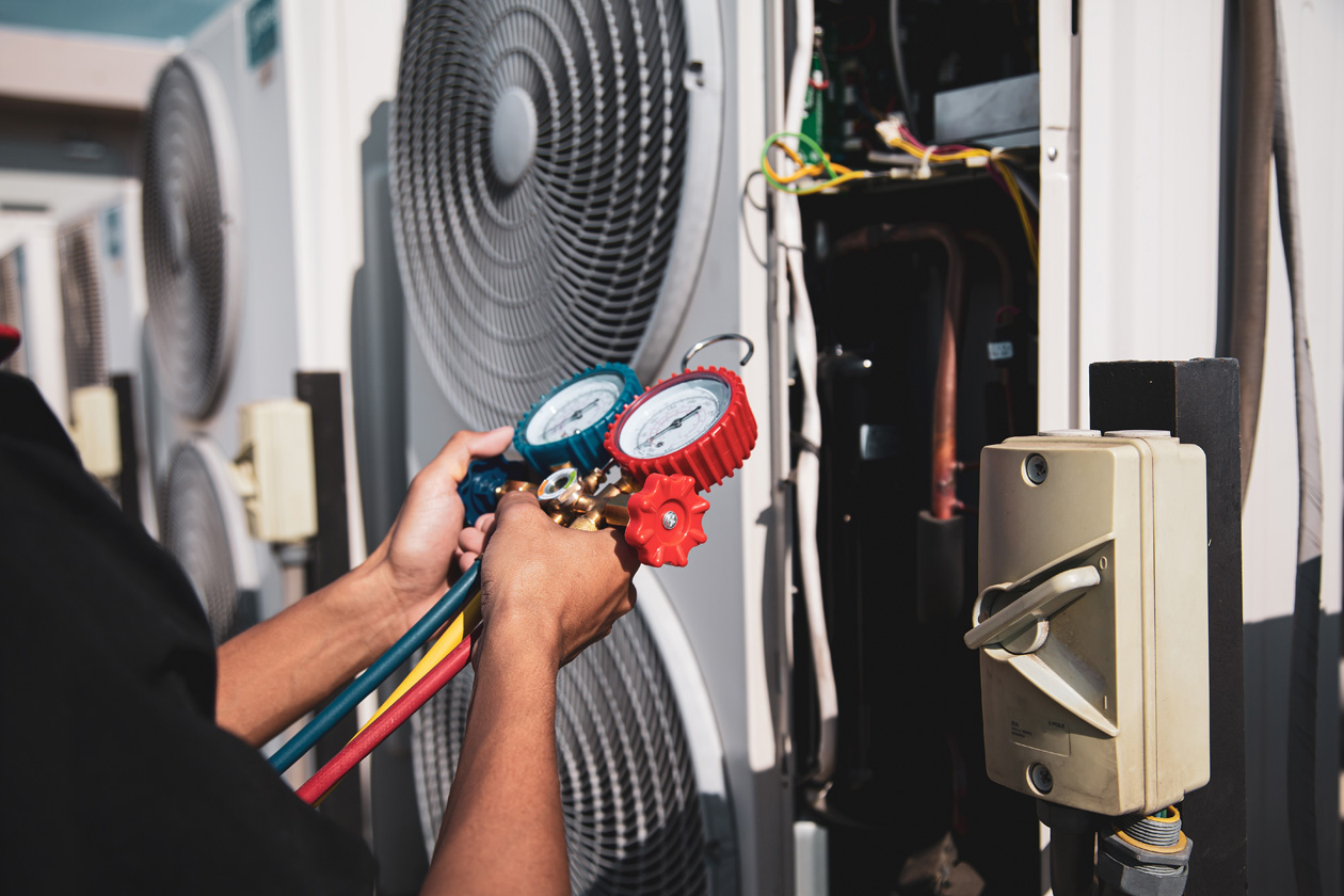 Technician using pressure gauges to inspect and repair a commercial HVAC unit outdoors
