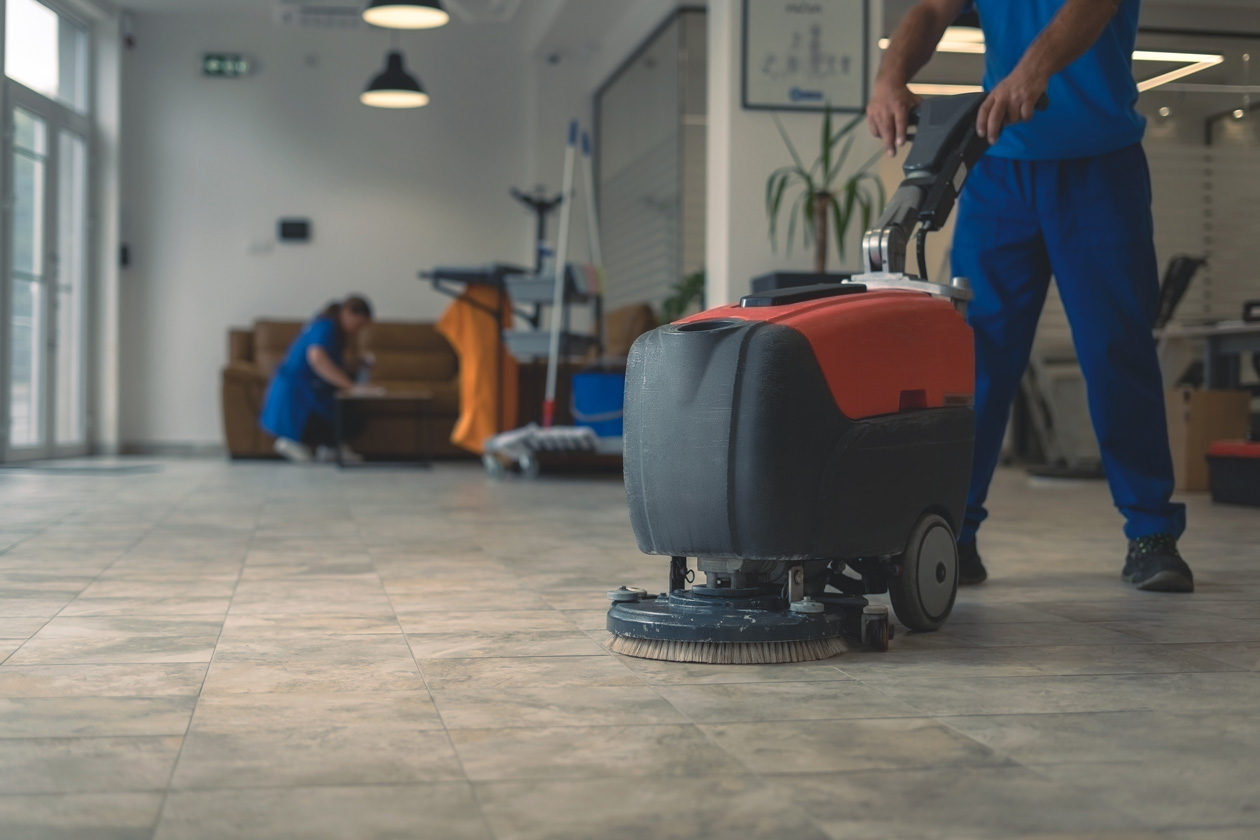 Cleaning professional using a floor scrubbing machine to restore and maintain hard surface flooring